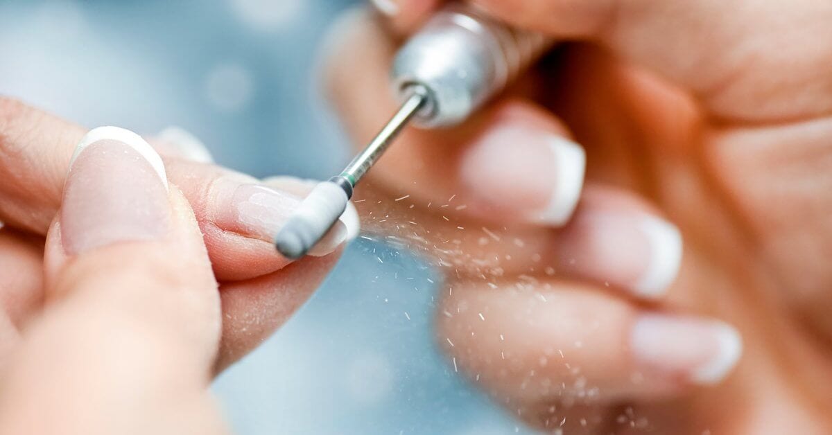  A close-up of a nail tech using an electric nail file drill on the customer's nails. The tech is filing off acrylic.